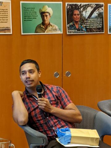 Photo of Luis Fernando Garcia Monroy speaking at UBC in front of photos of Xinca community members